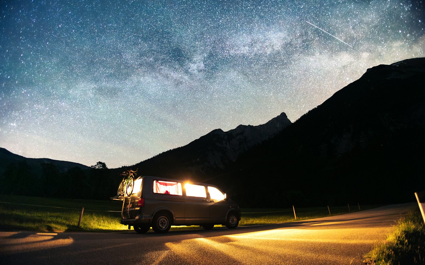 Furgoneta camper con luces encendidas aparcada junto a una carretera por la noche.