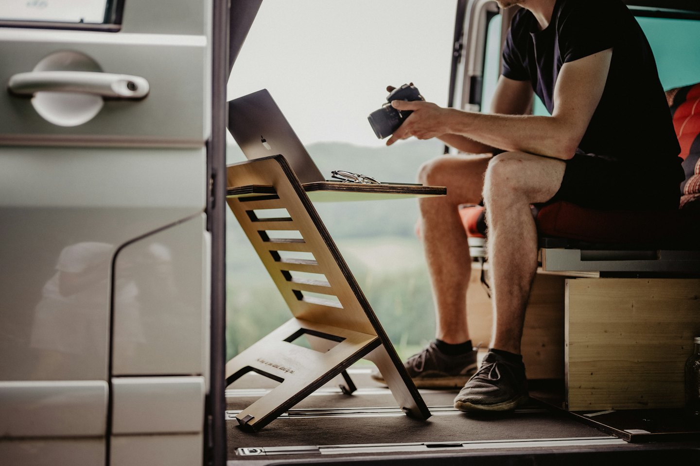 Persona trabajando remotamente desde una furgoneta camper con portátil y cámara.