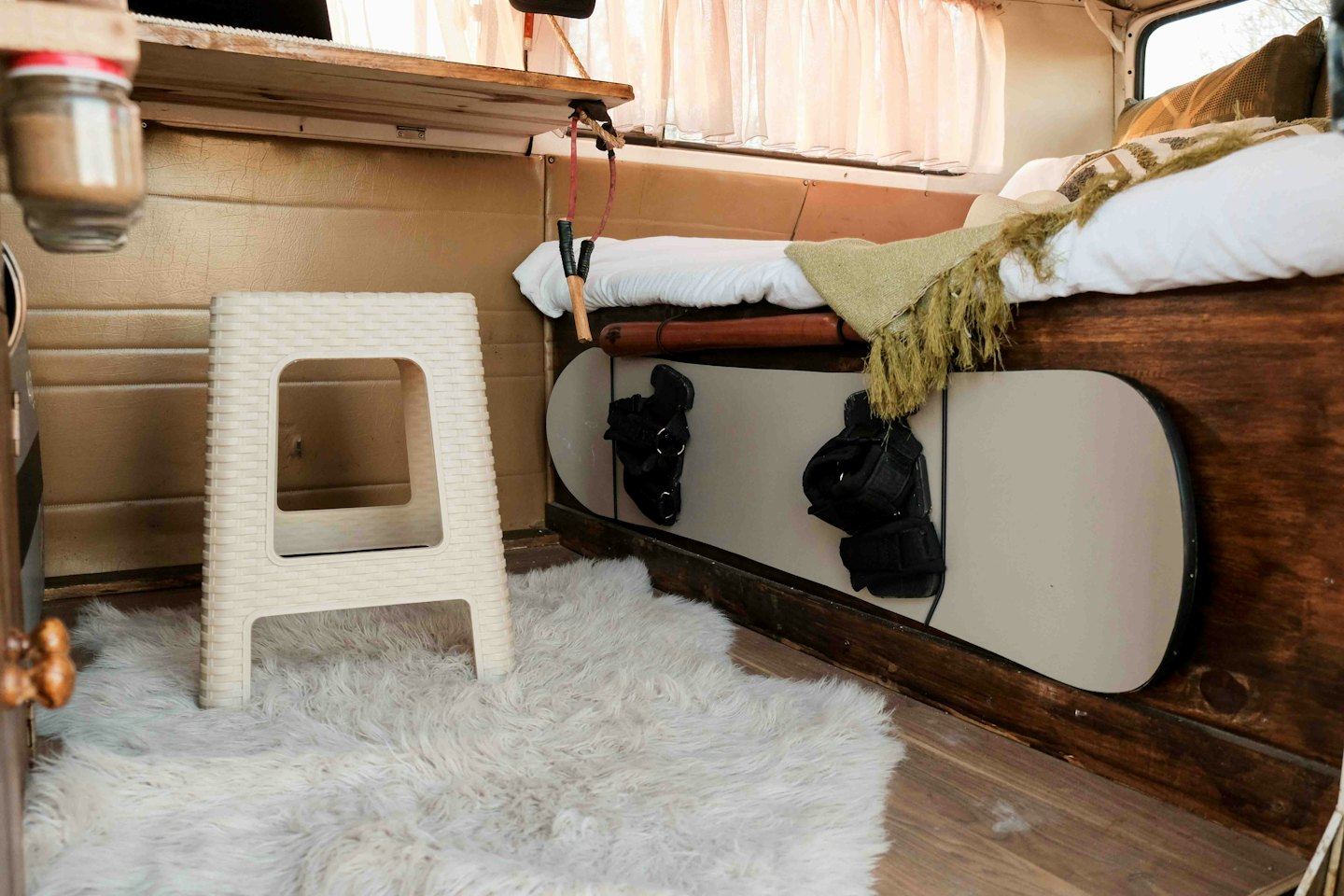 Tabla de snowboard guardada debajo de una cama hecha en una furgoneta camper rústica.