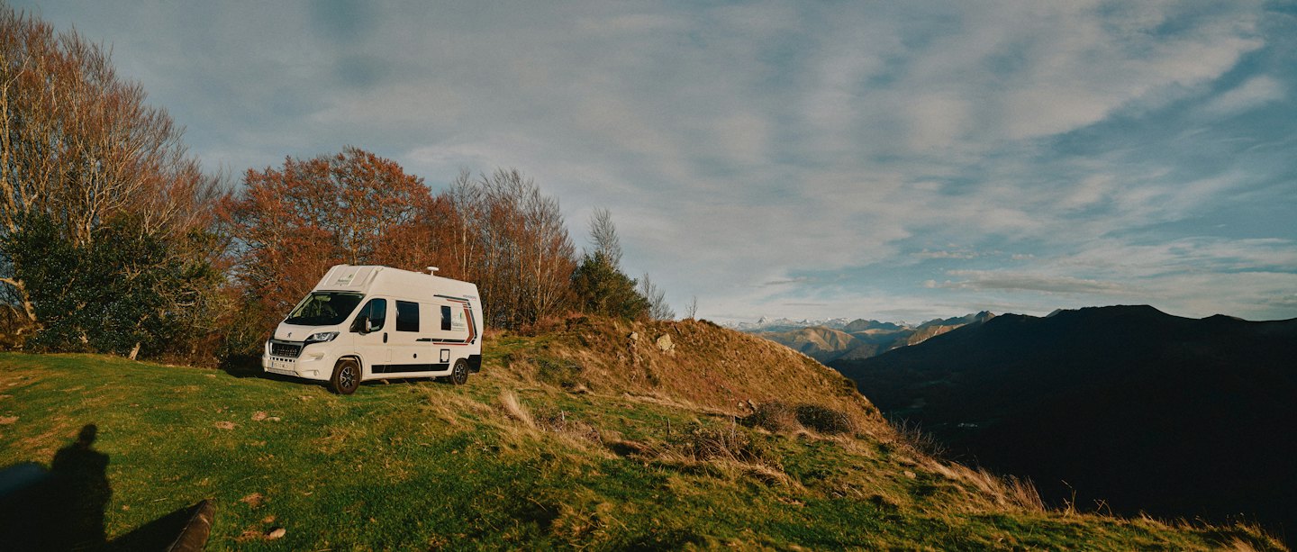 Una furgoneta camper blanca aparcada en una ladera de montaña cubierta de hierba.